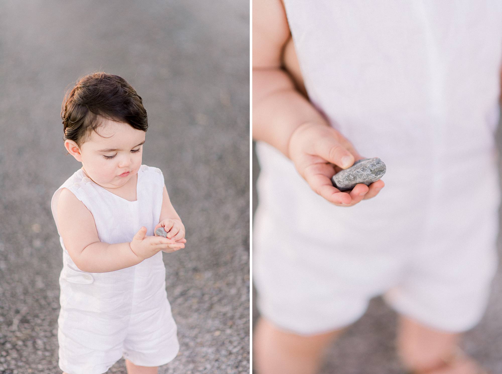 baby in white sunsuit holds rock