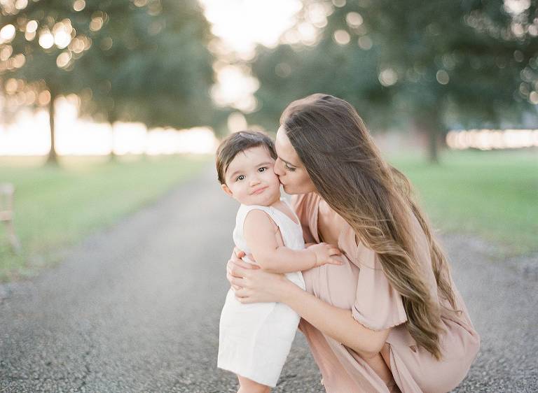 mom kisses baby's cheek as they stand in a oak lined alley