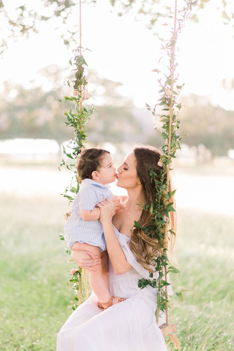baby and mom kisses on swing adorned in flowers