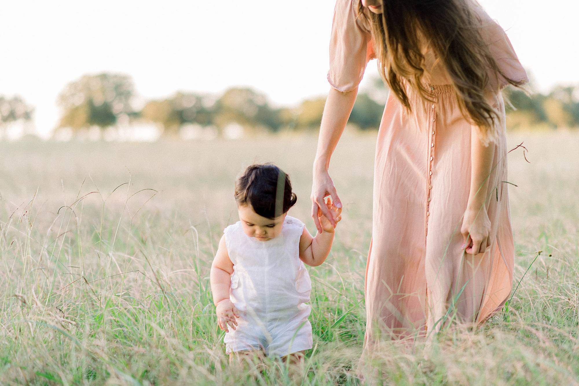 mother baby holding hands as they walk in a field