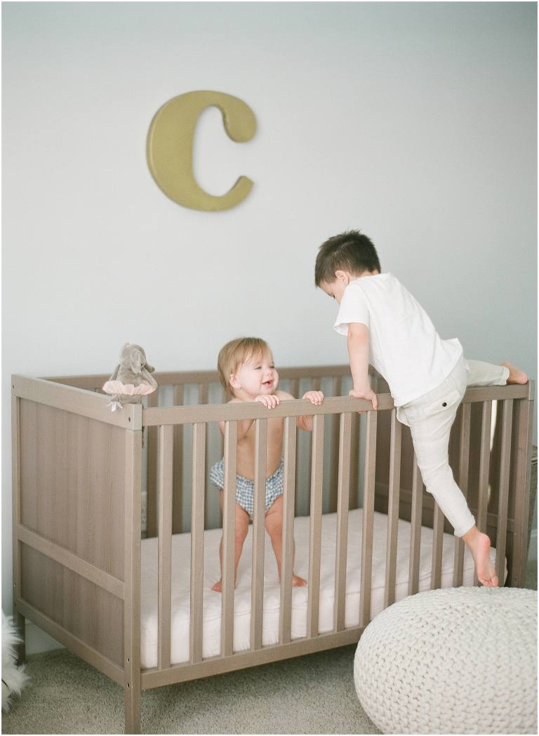 photographer captures sibling climbing into baby crib inside the nursery in lafayette la