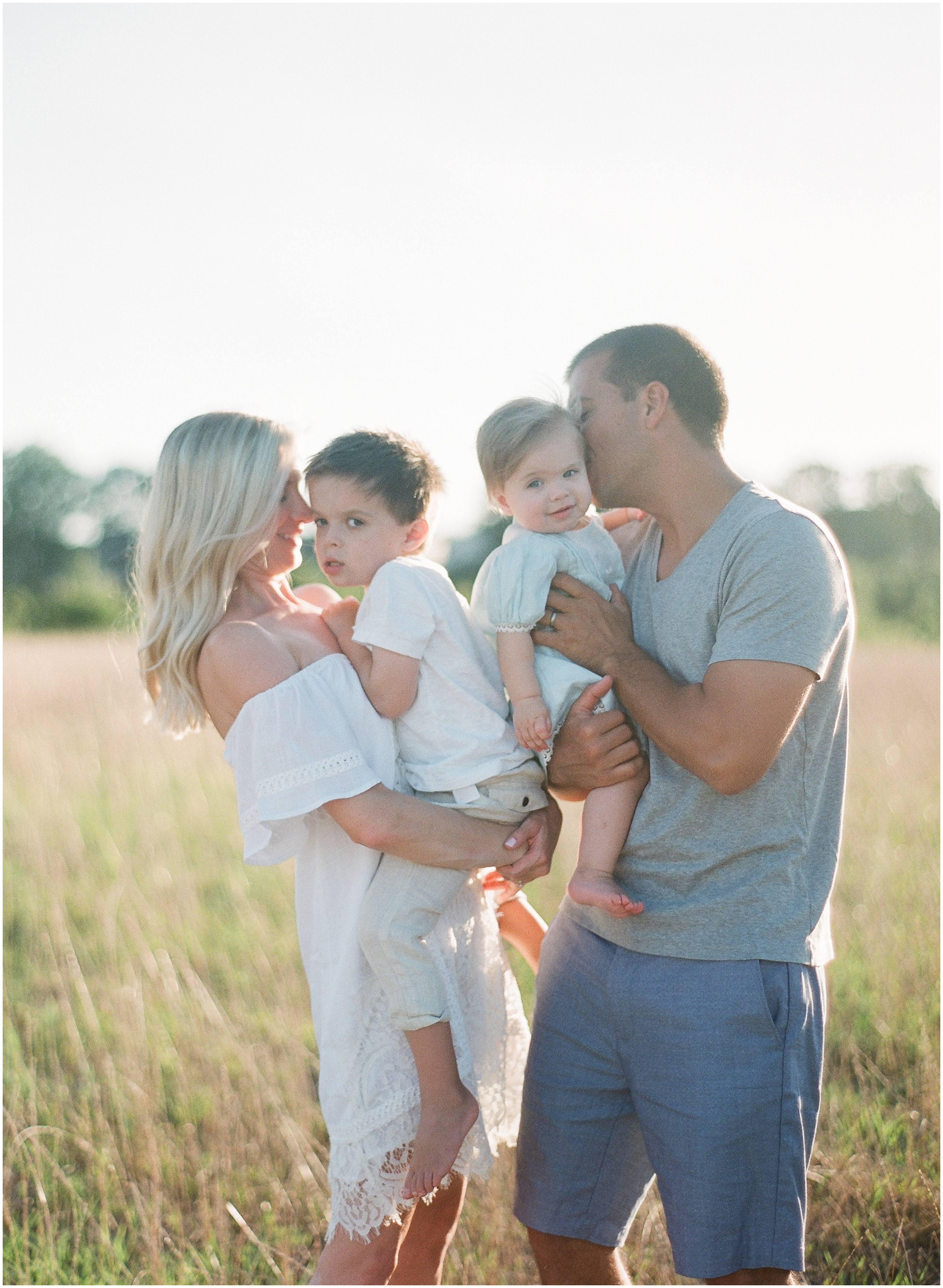 parents kiss their boy and girl photographed candidly outdoors by louisiana film photographer