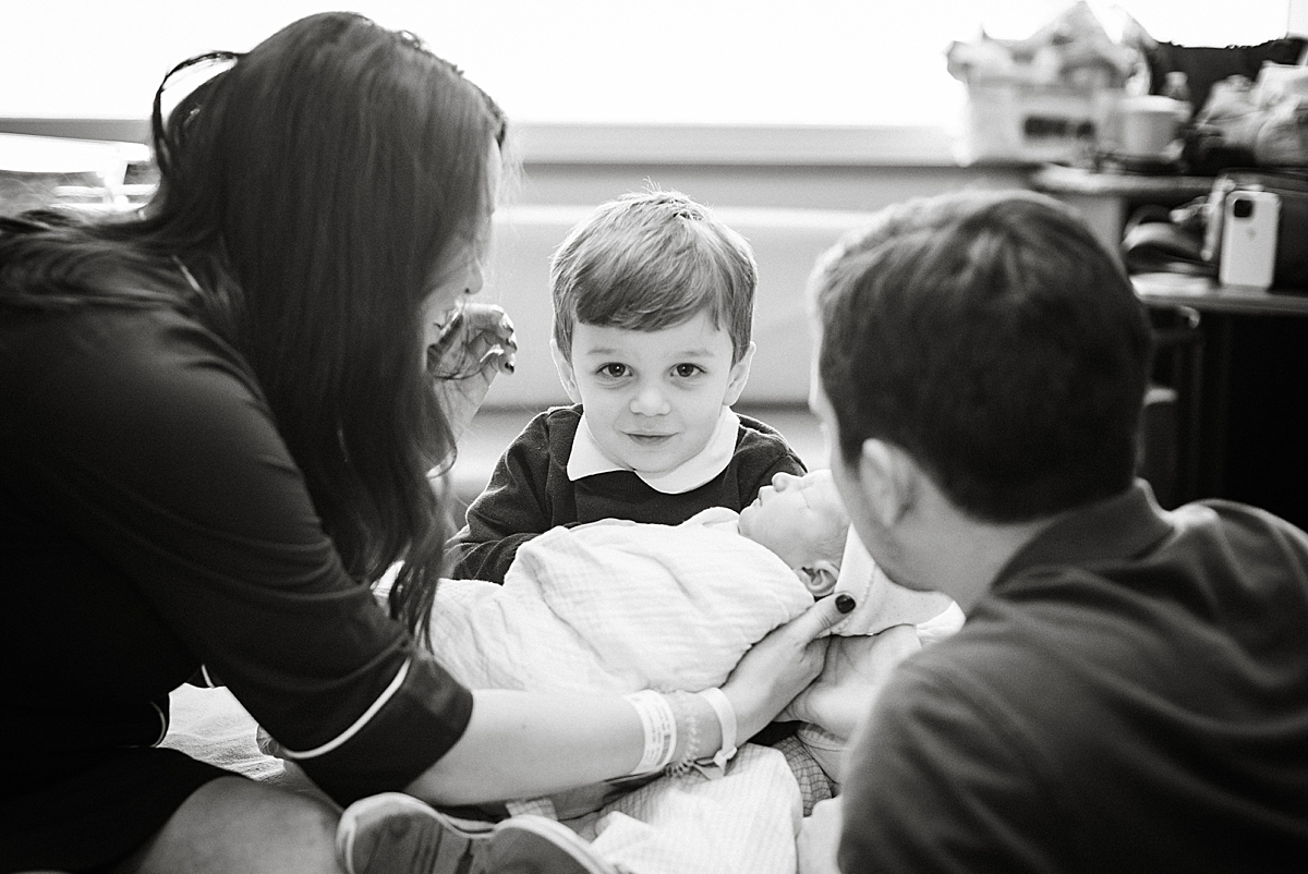 black and white image of big brother holding his new sibling in the hospital