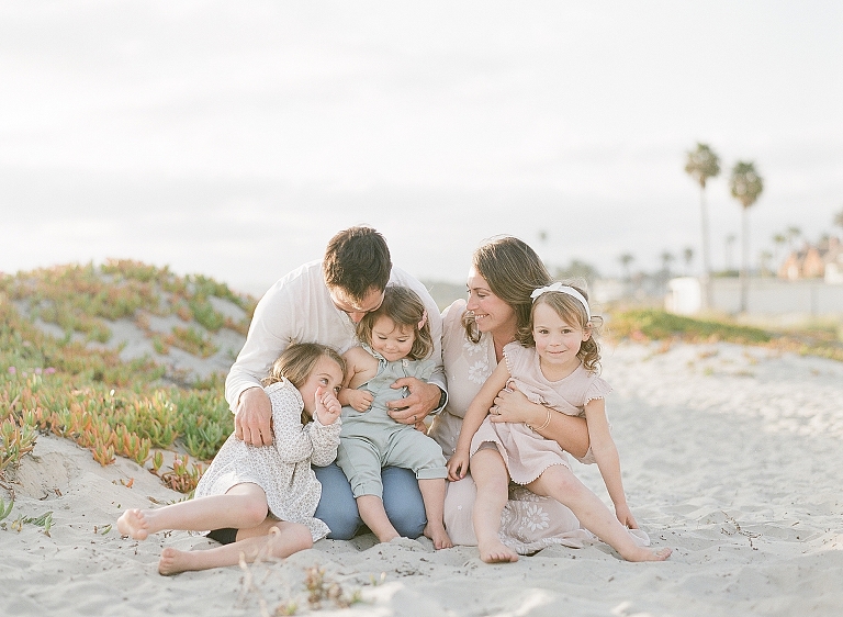 family of five snuggles and hugs on the beach of San Diego while they are getting photographed