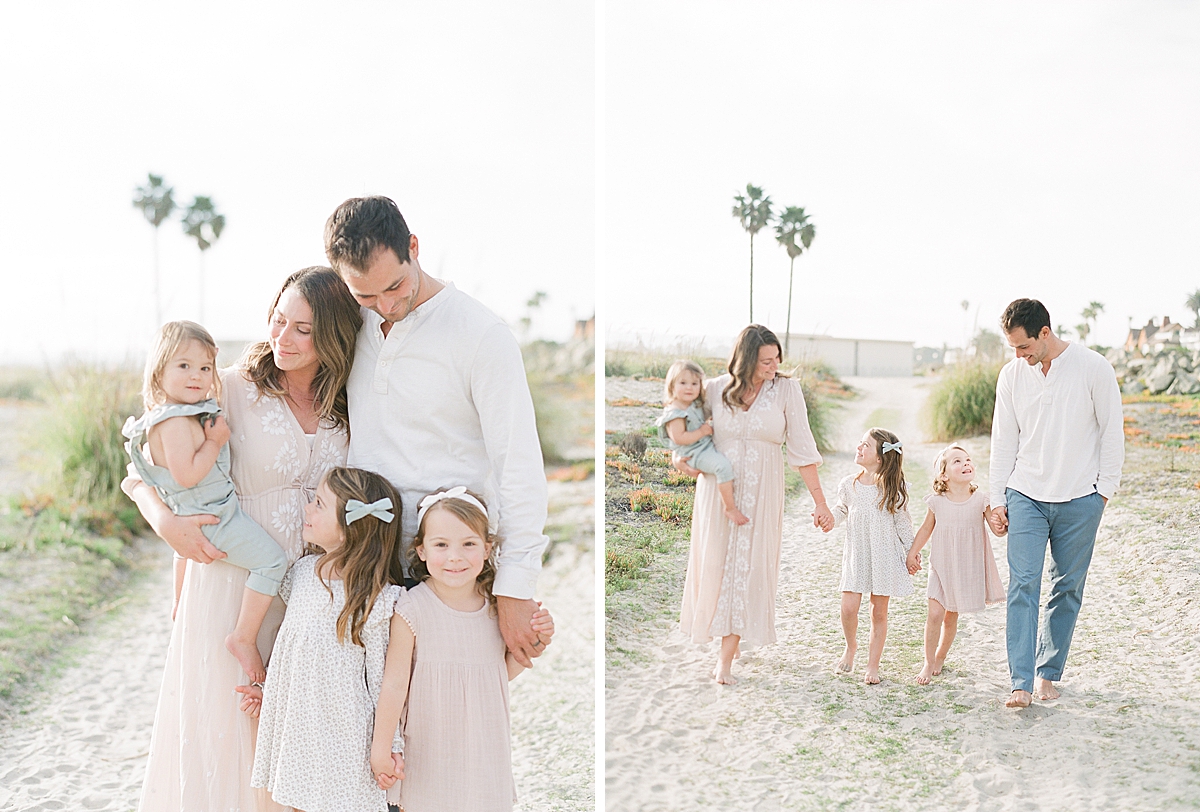 parents hold kids hands and walk with them down the beach smiling