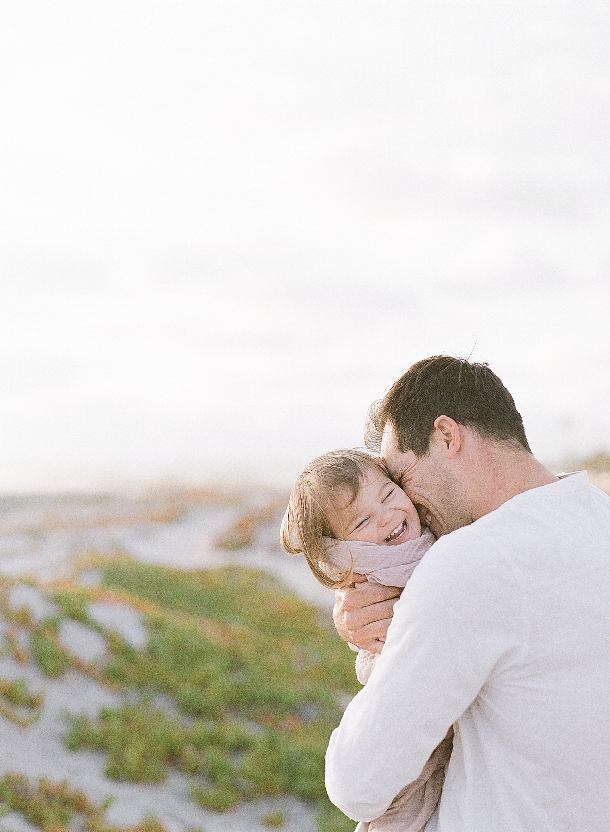 baby girl laughs as her dad tickles her on the beach in California during a photography session