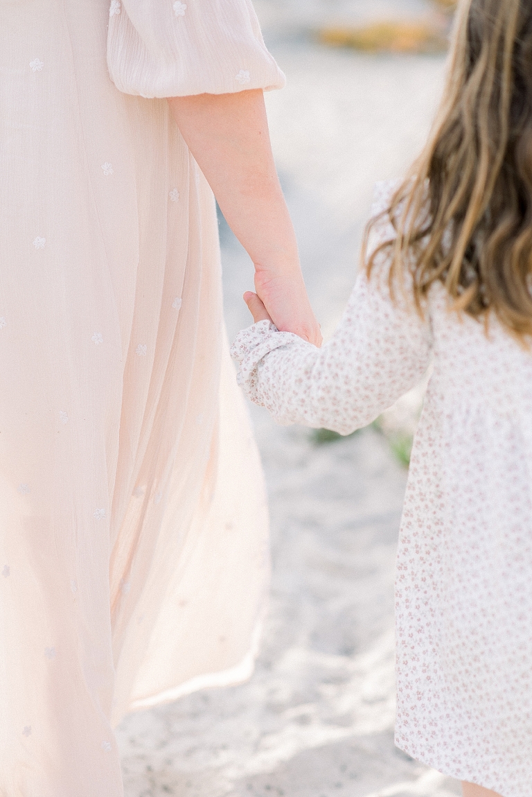 mom holds daughters hand for a detail portrait on the beach