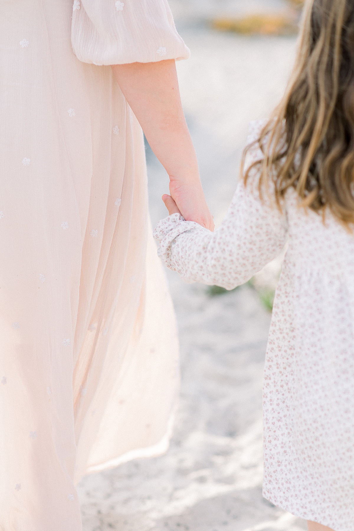 mom holds daughters hand for a detail portrait on the beach