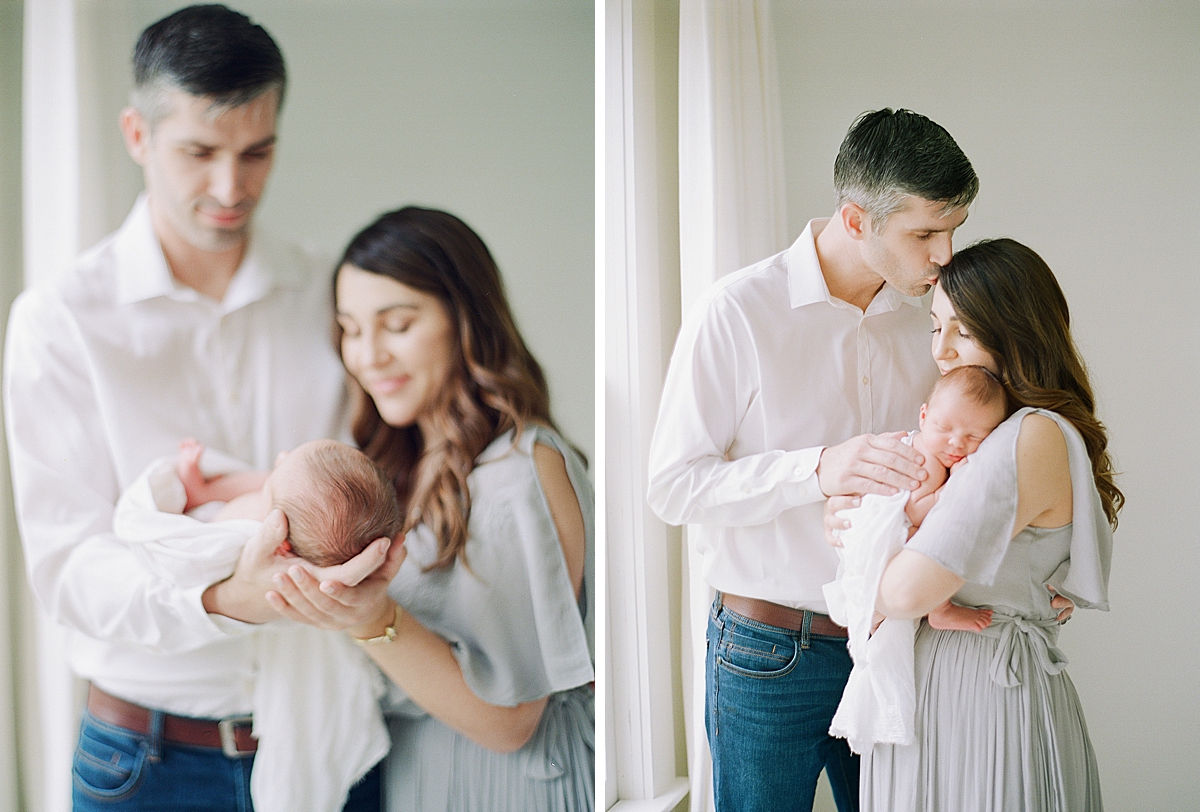 Newborn and parents holding baby in the natural light in home studio white walls and organic color pallet