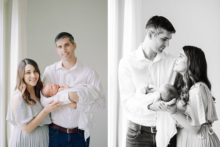 Parents smiling at camera holding newborn baby in a natural light photography studio