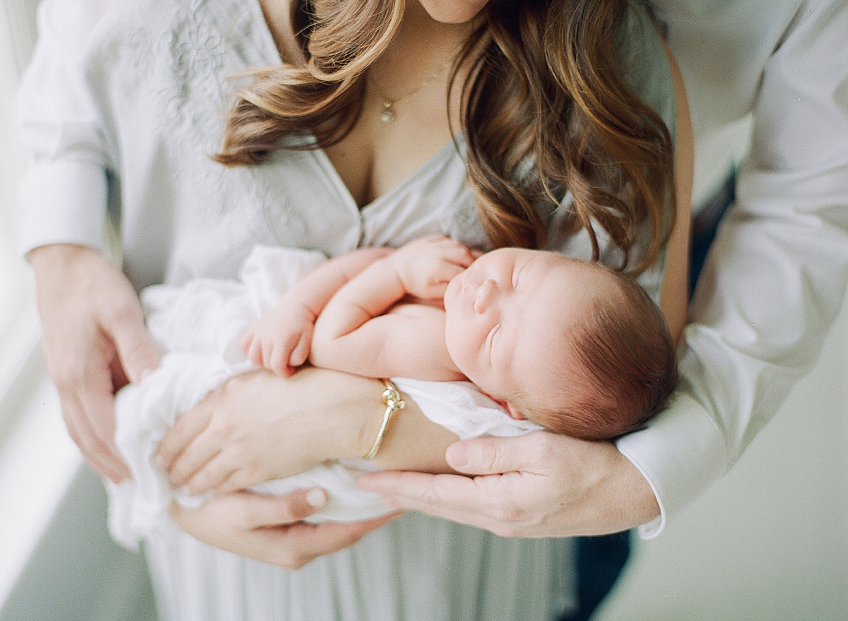 newborn baby sleeping in mothers arms as she rocks it to sleep during newborn photography session inside of studio