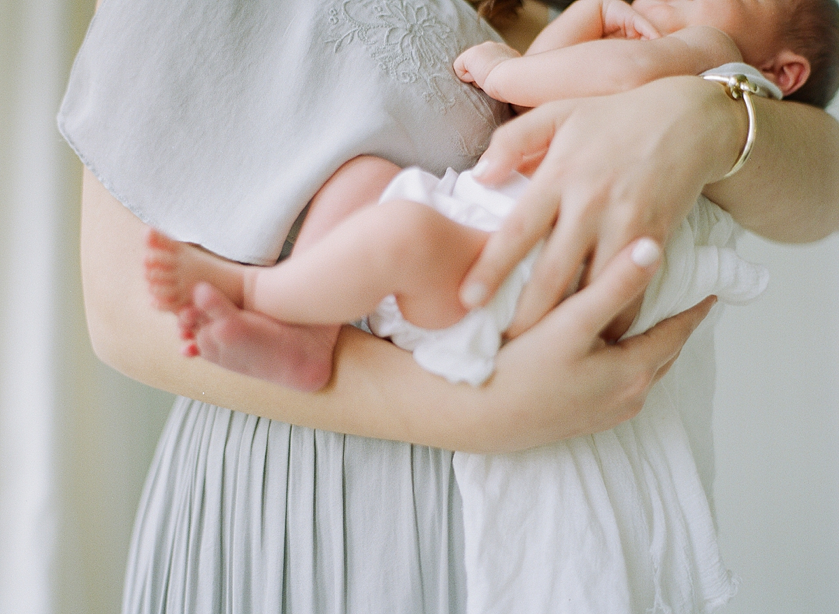 newborn baby held by mother and baby toes peeping out of the blanket