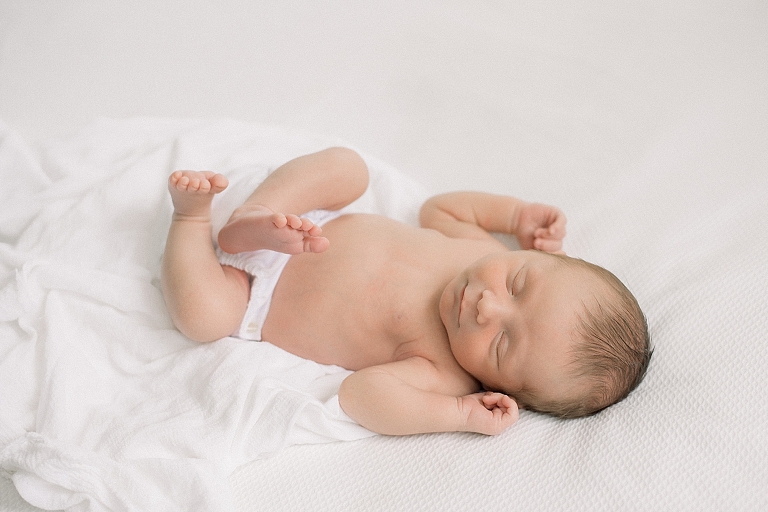 newborn baby boy sleeping in a heirloom diaper cover on all white bed in photography studio