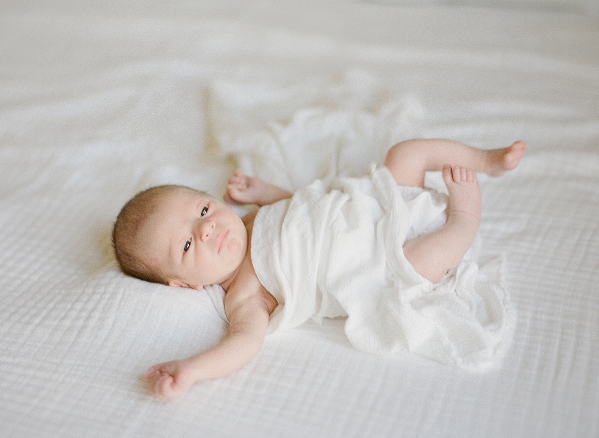 rainbow baby, newborn boy wrapped in muslin white gauze blanket as he is wide eyed and bush tailed kicking his feet into the air