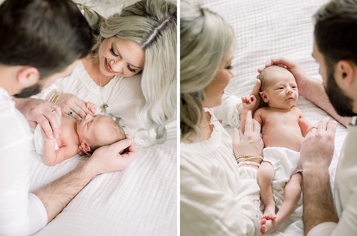 parents cup newborn baby's head into their hands as they hold him, he is staring right up at them with a grim