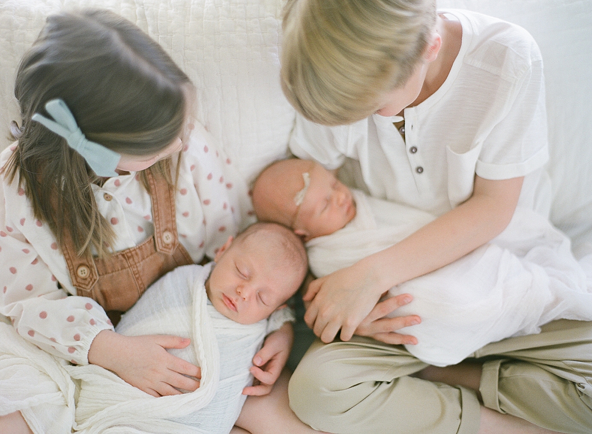 older siblings rock their newborn twin baby brother and sister to sleep at their lifestyle newborn photography session in studio