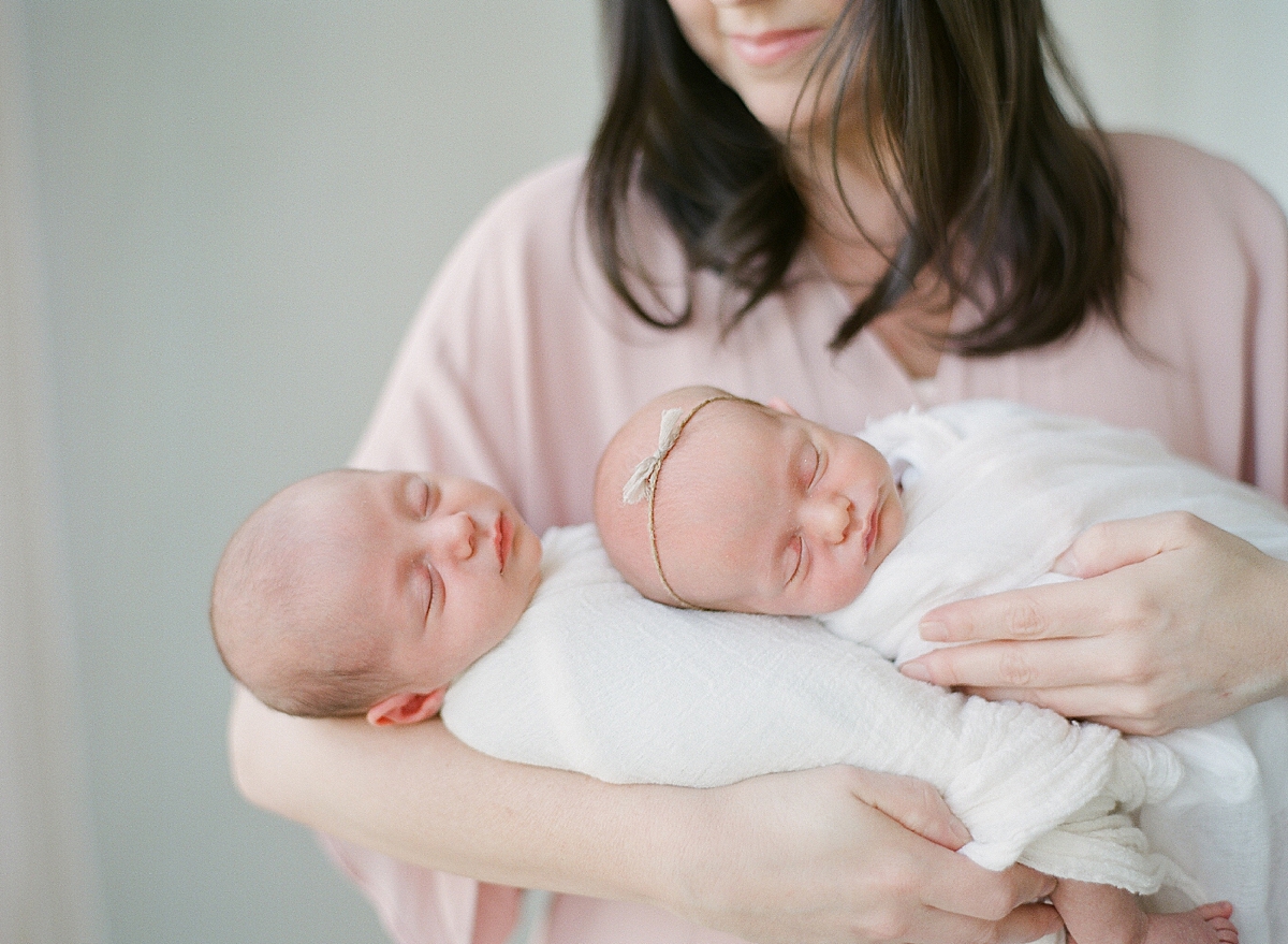 mother hold both swaddled newborn twins as they sleep in her arms