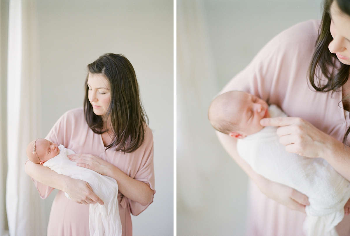 Mom brushes newborns cheek and rocks it to sleep as she holds her girl newborn twin during lifestyle newborn photography session