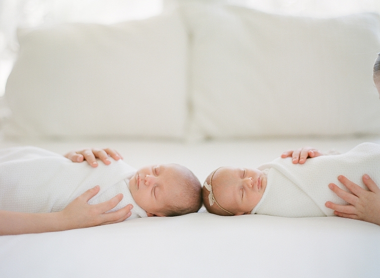 detail portrait of big siblings hands holding newborn twins as they lay on the bed sleeping swaddled 
