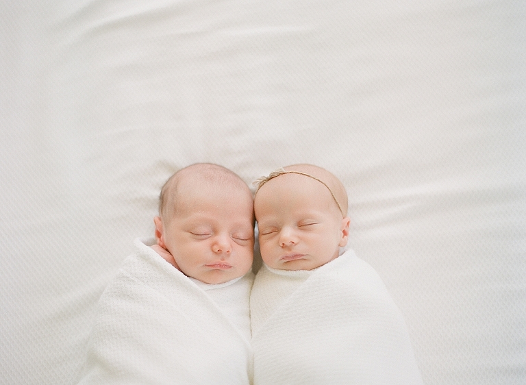 newborn boy girl twins laying on white bed as they sleep together wrapped in a white blanket