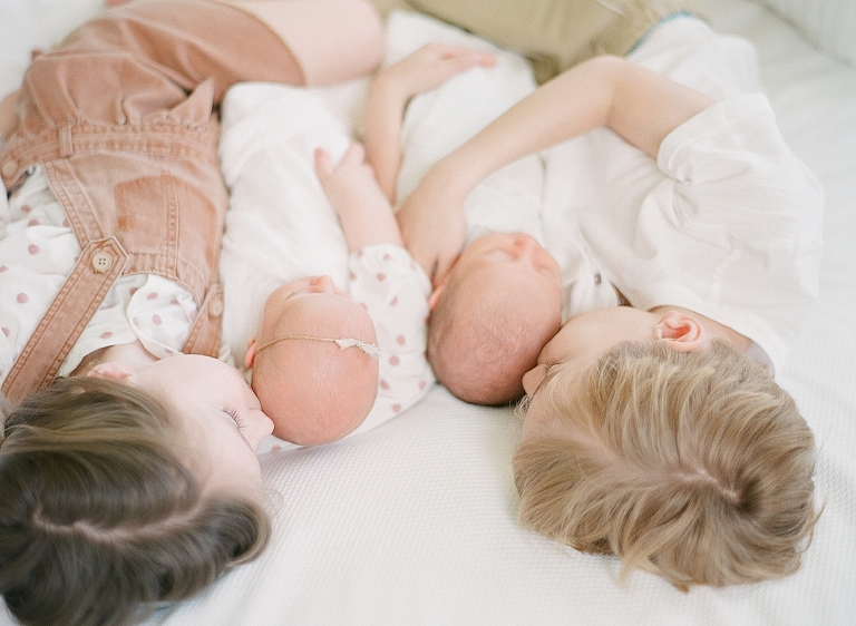 brother and sister hold their newborn twin siblings on the bed and give them soft kisses as they sleep
