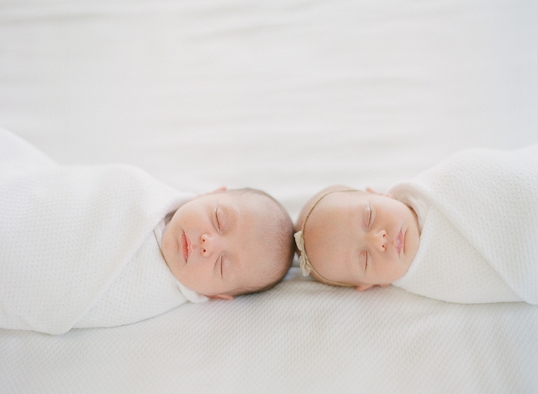 newborn fraternal boy and girl twins lay together on bed wrapped in white swaddle 