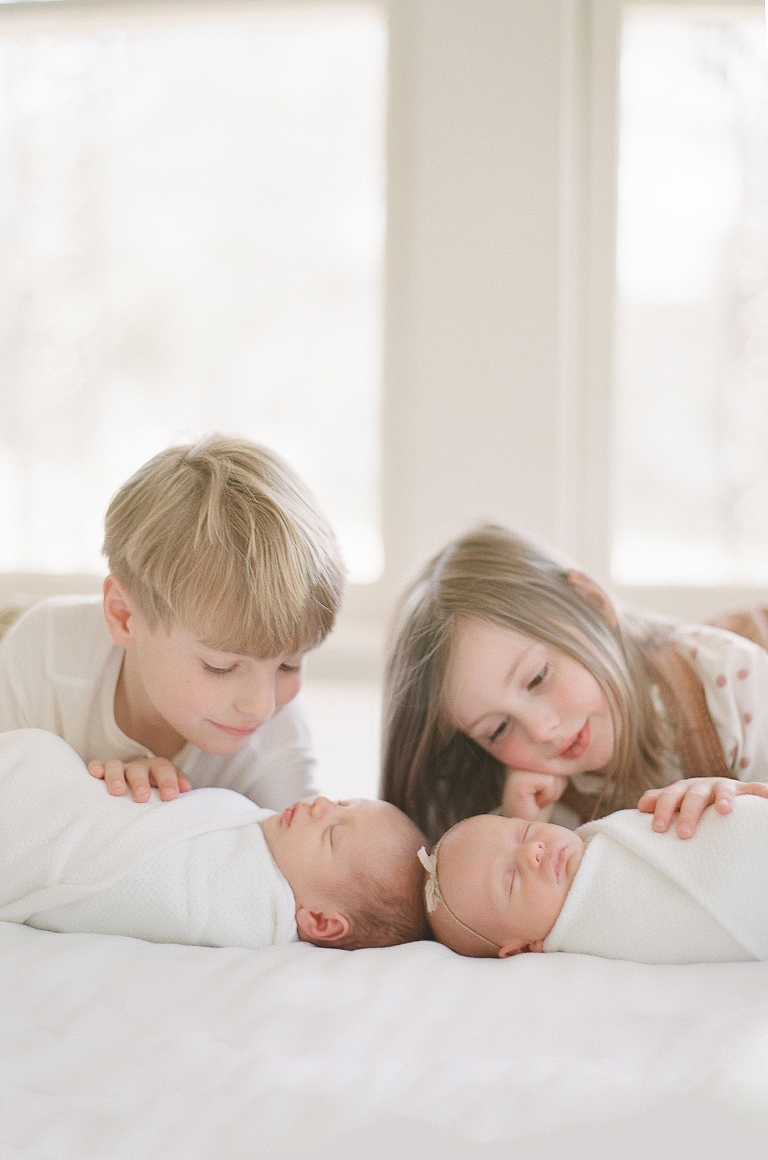 Brother and sister look down at newborn twin siblings in lifestyle newborn session