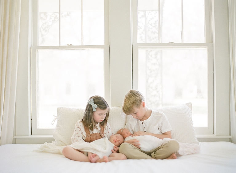 big brothers and sister hold newborn boy and girl twins at their newborn session in studio