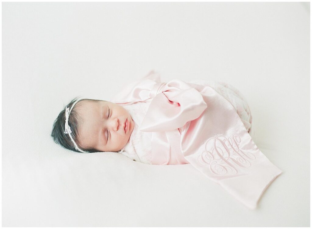 Newborn baby girl swaddled in a Beaufort Bonnet Company wrap adorned with her initials monogrammed on the bow swaddle 
